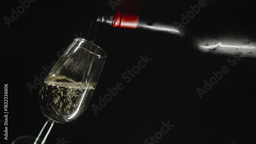 Filling a glass of manzanilla wine from a bottle against a black background