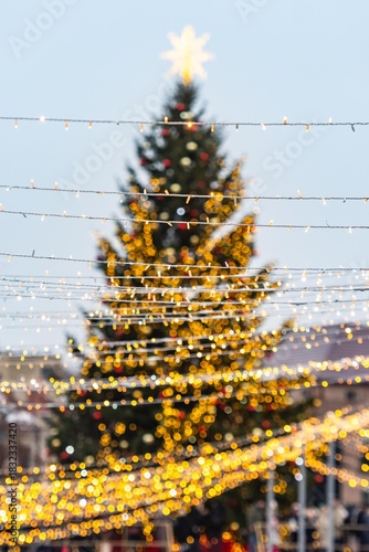 A large outdoor beautiful Christmas tree in Vilnius, decorated with warm white lights and ornaments, topped with a glowing star, standing in a festive setting with strings of lights in the foreground
