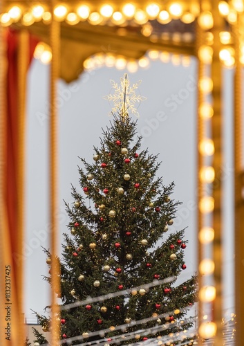 A large outdoor Christmas tree in Vilnius, decorated with warm white lights and ornaments, topped with a glowing star, standing in a festive setting with strings of lights in the foreground