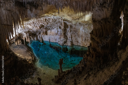 Large underground chamber filled with dense stalactites and rock formations, illuminated by soft artificial light inside a deep limestone cave
