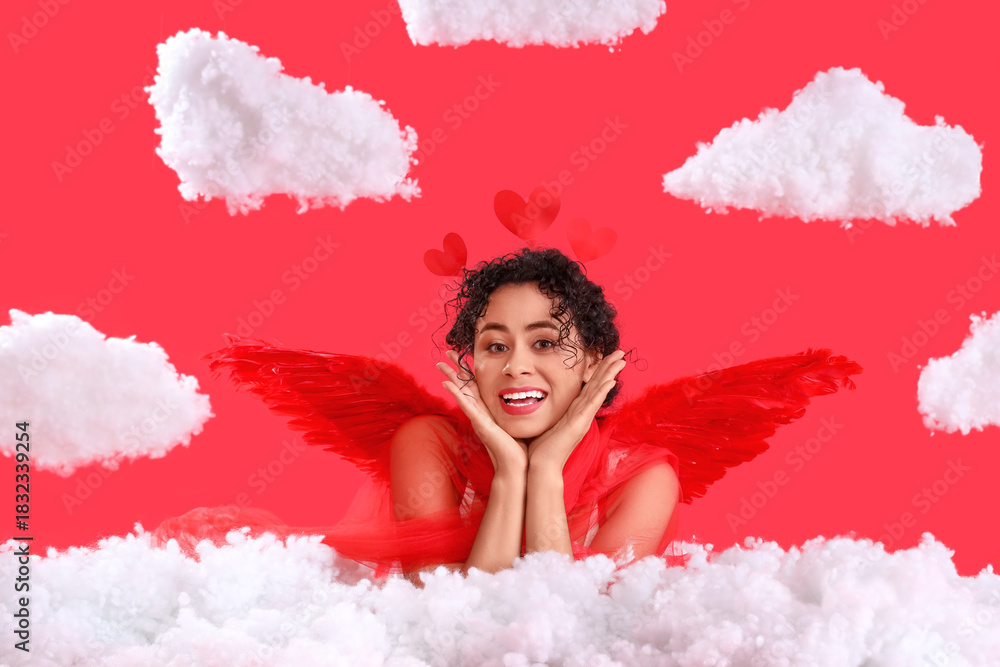 Fototapeta premium Young African-American woman dressed as Cupid in clouds on red background. Valentine's Day celebration