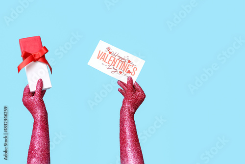 Painted female hands with gift and card for Valentine's Day celebration on color background, closeup