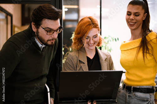Group of three professionals collaborating in a modern workspace while looking at a laptop screen during a team meeting in the afternoon light