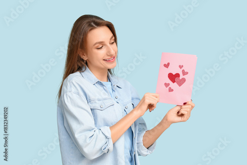 Beautiful young woman holding greeting card with hearts on blue background. Valentine's Day celebration