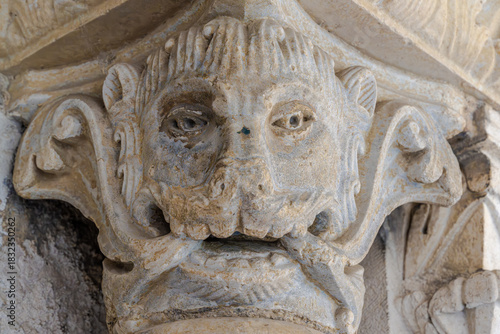 Arles, Saint-Trophime cloister, Provence, France: close-up fine art view of a Romanesque sculpted mascaron on a medieval capital. Detailed stone texture revealing ancient craftsmanship.