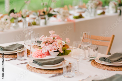 Coziness and style. Modern event design. Table setting at wedding reception. Floral compositions with beautiful flowers and greenery, candles, laying and plates on decorated table.