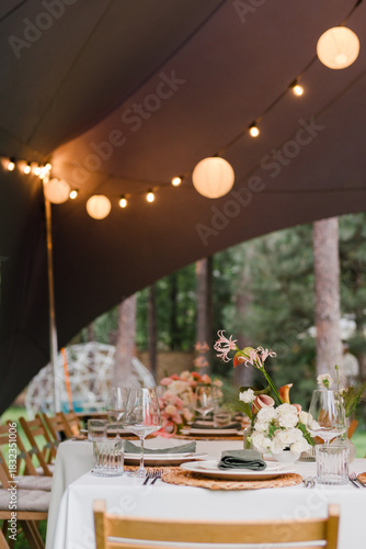 Coziness and style. Modern event design. Table setting at wedding reception. Floral compositions with beautiful flowers and greenery, candles, laying and plates on decorated table.