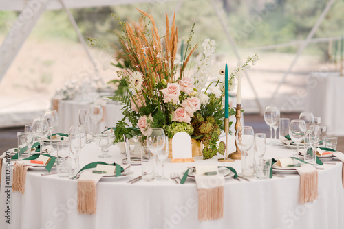 Coziness and style. Modern event design. Table setting at wedding reception. Floral compositions with beautiful flowers and greenery, candles, laying and plates on decorated table.