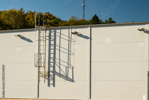Industrial wall with metal safety ladder casting long shadow in sunlight.