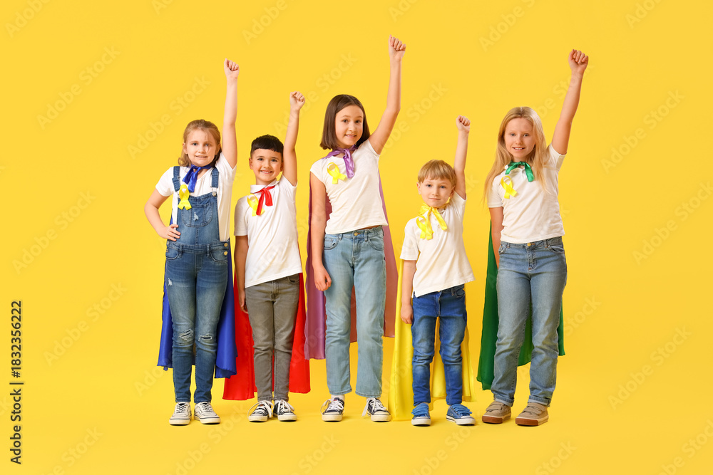 Fototapeta premium Little children dressed as superheroes with gold ribbons on color background. Childhood cancer awareness concept
