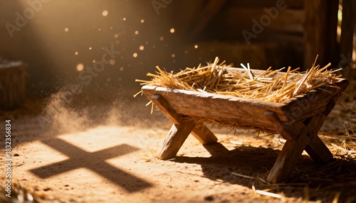 Wooden manger with straw in a rustic stable illuminated by a divine beam of light. Shadow on the ground forms a Christian cross. Nativity and Christmas concept