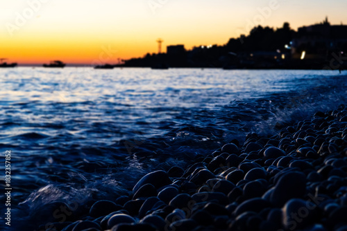 Pebble beach at beautiful sunset with waves and twilight sky, scenic coastal seascape for summer travel