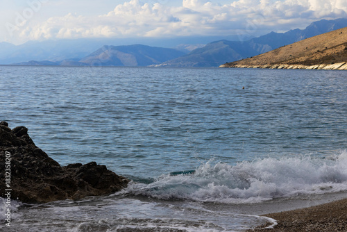 Scenic view near Himare on the Albanian Riviera, with waves, rocks, clouds, and distant mountains