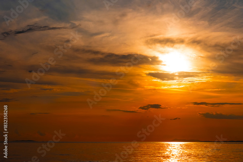 Dramatic sunset over the sea with glowing sun descending into clouds above distant islands