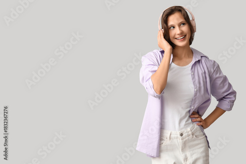 Smiling young woman in modern headphones on grey background