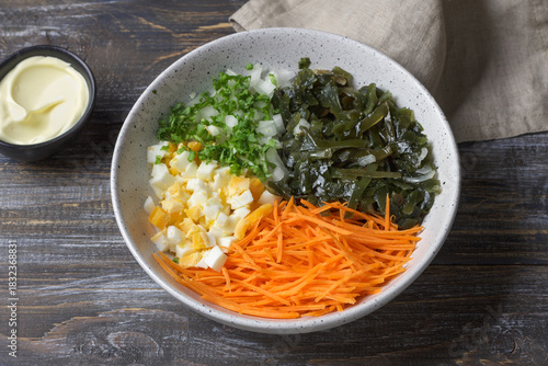 Ingredients for seaweed salad: seaweed, shredded carrots, chopped eggs, herbs and onions in a ceramic bowl on a rustic wooden surface 