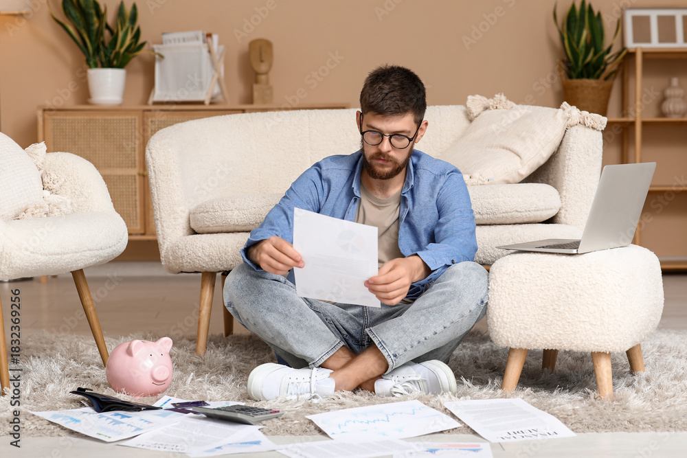 Fototapeta premium Young man in debt with paper sitting on floor at home