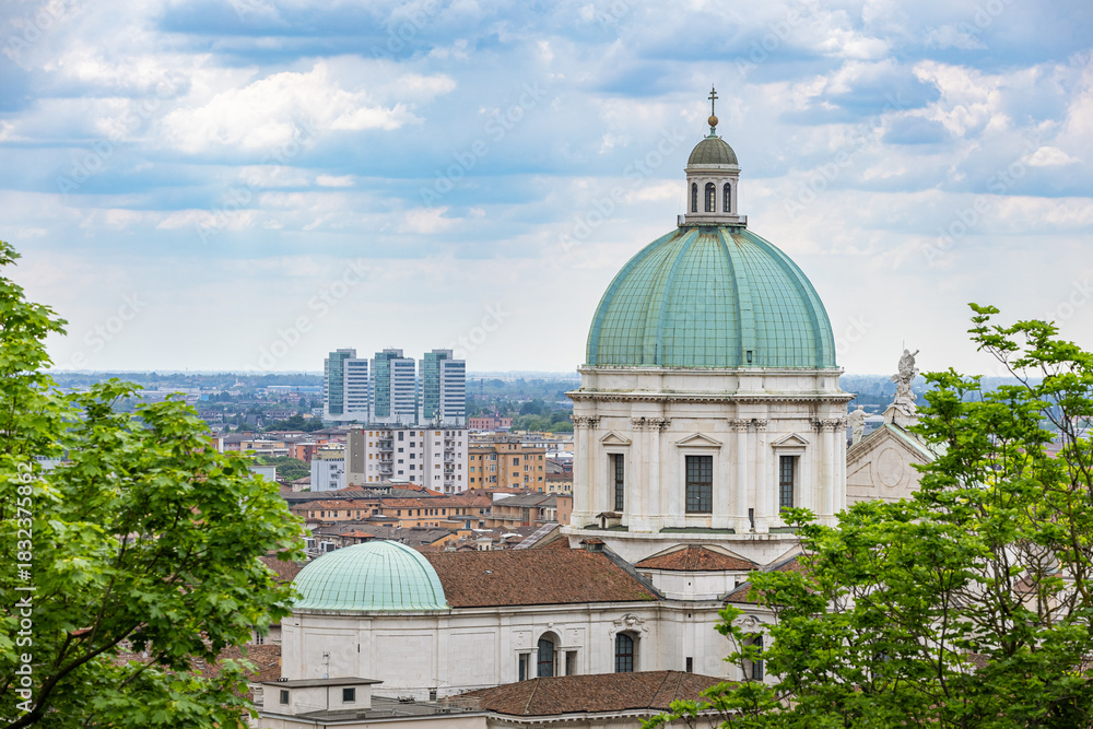 Fototapeta premium View of the green dome of the Sanctuary of Santa Maria delle Grazie (or a similar church) overlooking the cityscape of Brescia, with modern high-rise buildings visible in the distance