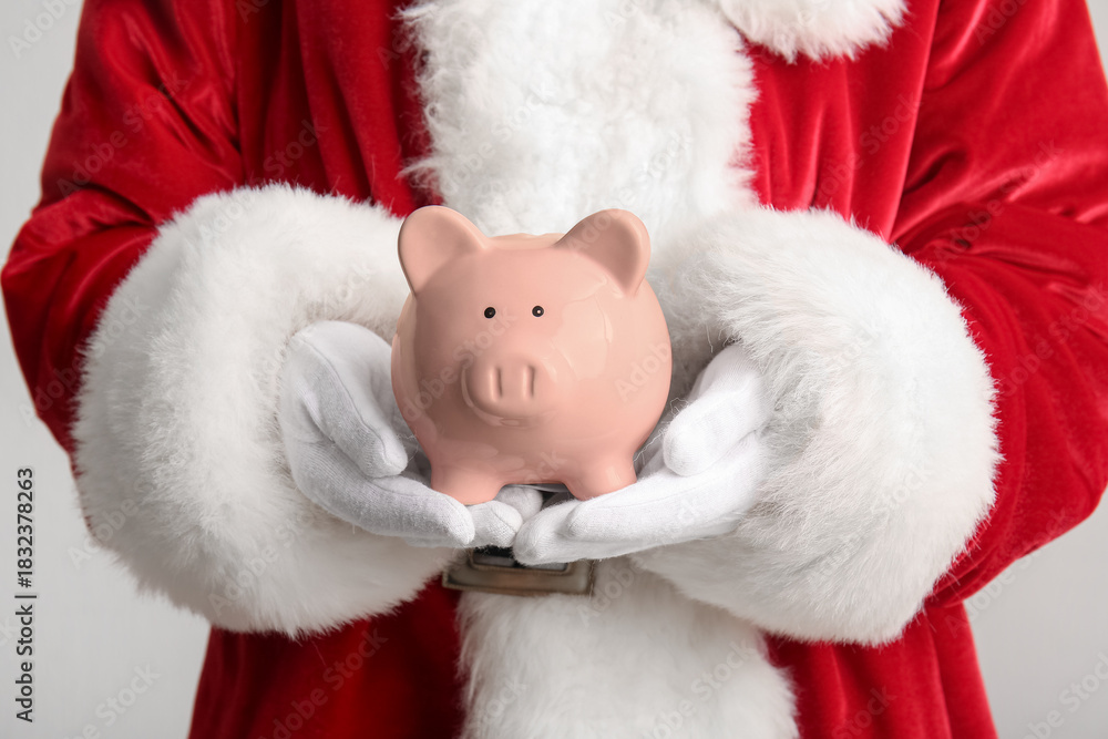 Fototapeta premium Santa Claus with piggy bank on light background, closeup