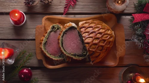 Top view of placing a plate with juicy Beef Wellington slices on a rough wooden table. Decorated with Christmas ornaments in a rustic style. Festive holiday dinner