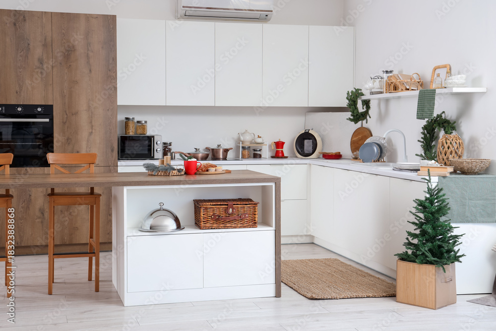 Fototapeta premium Interior of festive kitchen with white counters, Christmas decorations and fir tree