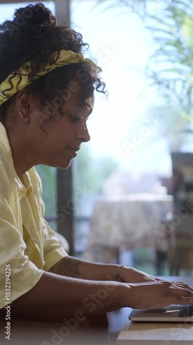 Vertical. African millennial woman works on a laptop at home, symbolizing freelance business, online shopping, digital learning, and the modern lifestyle of remote connectivity.