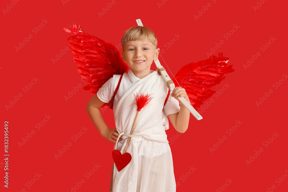Fototapeta premium Cute little happy boy dressed as cupid with bow and arrow on red background. Valentine's Day celebration