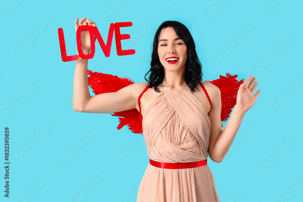 Fototapeta premium Beautiful young happy woman dressed as cupid with word LOVE on blue background. Valentine's Day celebration