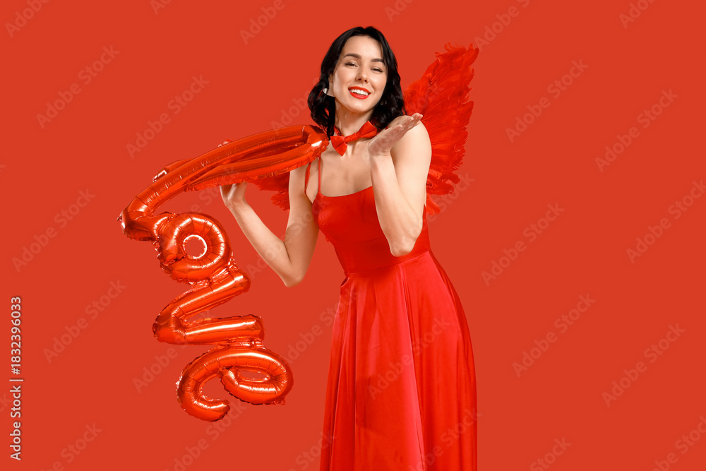 Fototapeta premium Beautiful young happy woman dressed as cupid with word LOVE made of balloons on red background. Valentine's Day celebration
