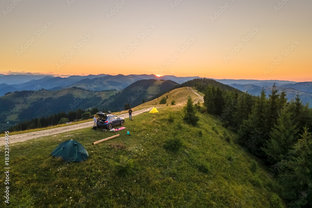 Fototapeta premium Sunset mountain landscape with tourist camping tents and a SUV car on hillside campsite at bright sunny evening. Offroad adventure