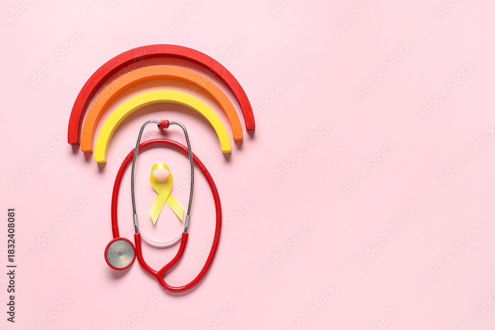 Obraz premium Yellow ribbon, toy rainbow and stethoscope on pink background. Childhood cancer awareness concept