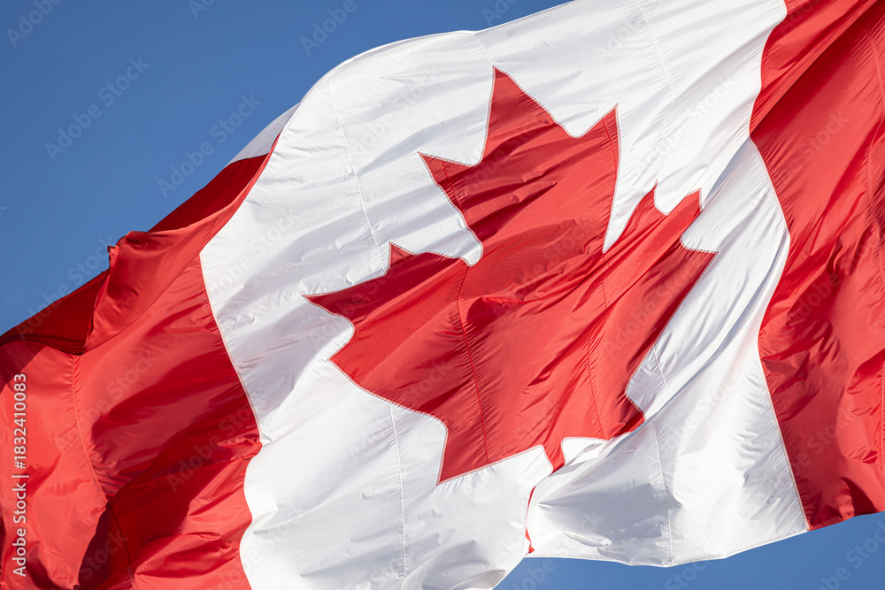 Fototapeta premium Red and white Canadian flag with a maple leaf waving in the air in downtown Toronto near Ontario Lake. Canadian patriotism and culture
