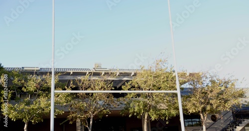 Framing pair of tall white goalposts dominating stadium exterior, showing covered stands