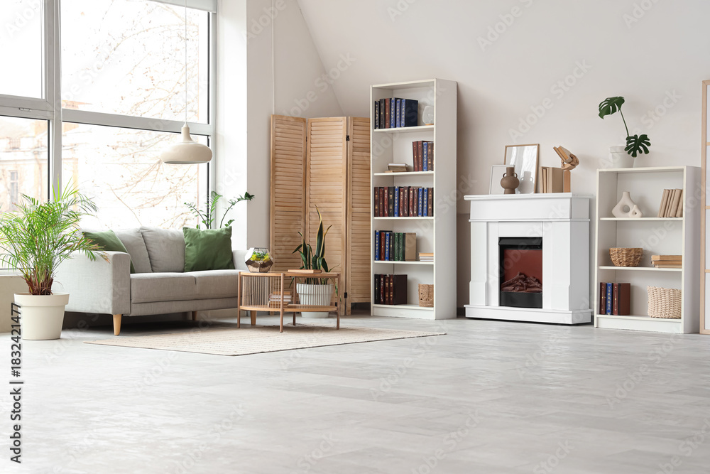Fototapeta premium Shelving units with books, fireplace, sofa and coffee table in interior of stylish living room