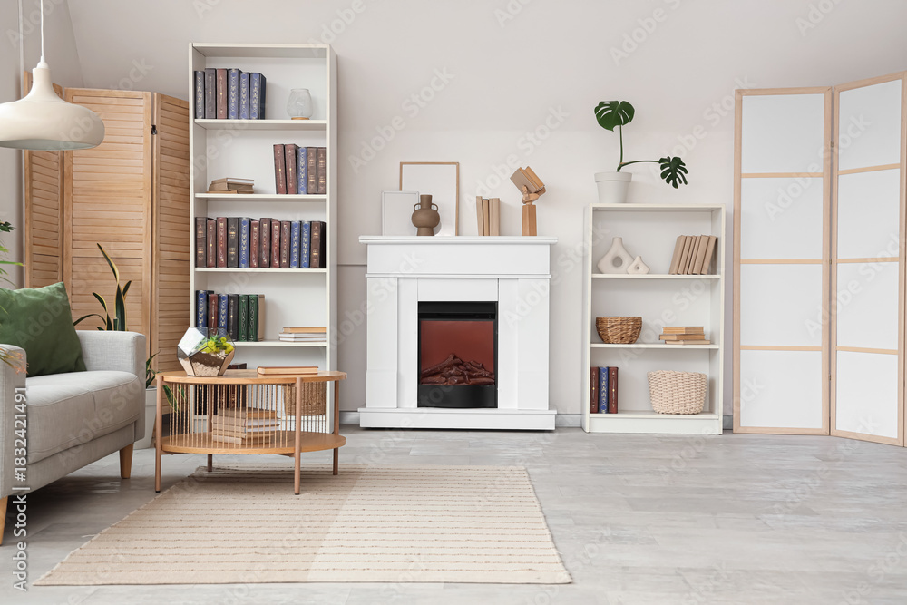 Fototapeta premium Shelving units with books, fireplace, sofa and coffee table in interior of stylish living room