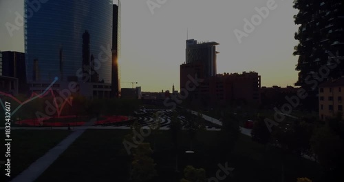 Sun emerging behind central midrise casting glare, glinting glass, revealing plaza, graphs sweeping