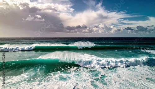 Dramatic view of ocean waves breaking on the surface under a cloudy sky. The turquoise water and white foam create a dynamic scene.