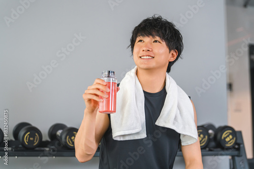 A young Asian man drinking EAA, protein during breaks and intervals at a fitness gym (hydration)
