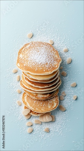 A stack of pancakes dusted with powdered sugar and scattered with sugar cubes on a light blue background. The image is a top-down shot.