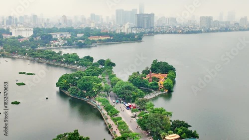 Aerial view of Hanoi city, Vietnam with road crossing the island lake with green tree lined street, temple located between small oasis.