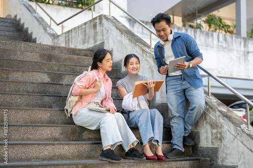 Foto Asian man student standing showing tablet to woman friends sitting on building stairs in university