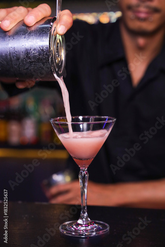 A bartender pouring a fresh cocktail from a shaker into a martini glass