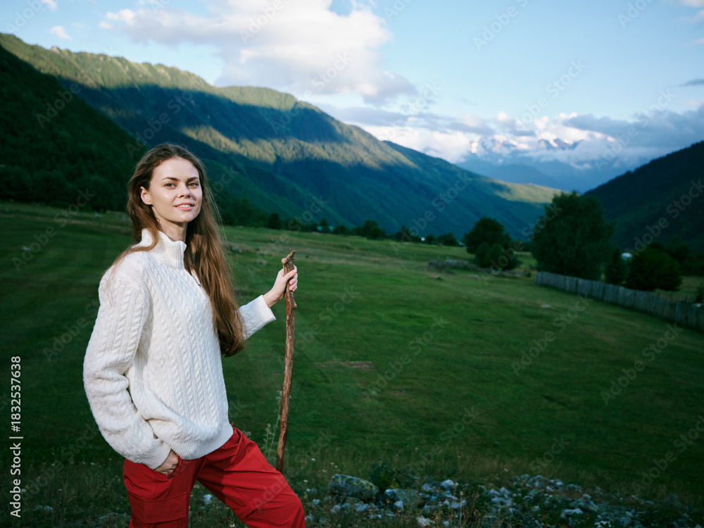 Fototapeta premium A young woman in a cozy white sweater stands in a lush valley with distant mountains, holding a rope, enjoying outdoor exploration and expansive natural scenery