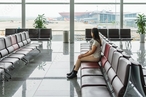 Casually dressed woman sits alone in the waiting area of a bright, modern airport terminal themes of international travel, business journey.