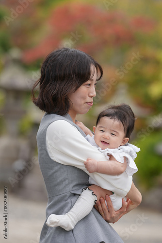 A woman is holding a baby in her arms. The baby is smiling and the woman is looking at the camera. The scene is peaceful and heartwarming, capturing a moment of love and connection between a mother