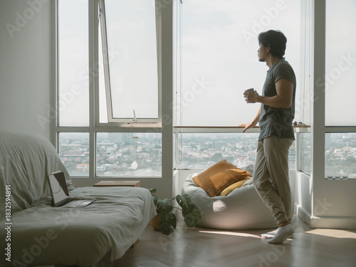 Asian man standing at the balcony looking at the view of the city, trying to relax from work problem.