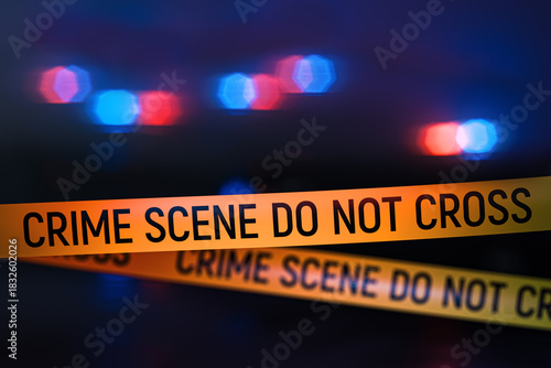 Closeup view of yellow crime scene tape with police car lights flashing in the background at night. Focus on the tape with bokeh, blur and lens glow creating dramatic investigation mood