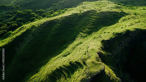 Aerial quadcopter view of a gentle mountain slope covered with grassy terraces forming soft waves in the landscape, creating a peaceful natural pattern with smooth elevation lines.