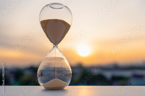 Hourglass with golden sand flowing at sunset symbolizing the end of the year and the beginning of a new one. Perfect for New Year reflections, countdowns, resolutions, and time concept backgrounds.