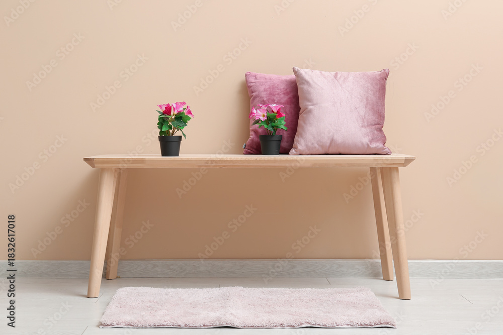 Naklejka premium Pink artificial flowers with pillows on table near beige wall in room